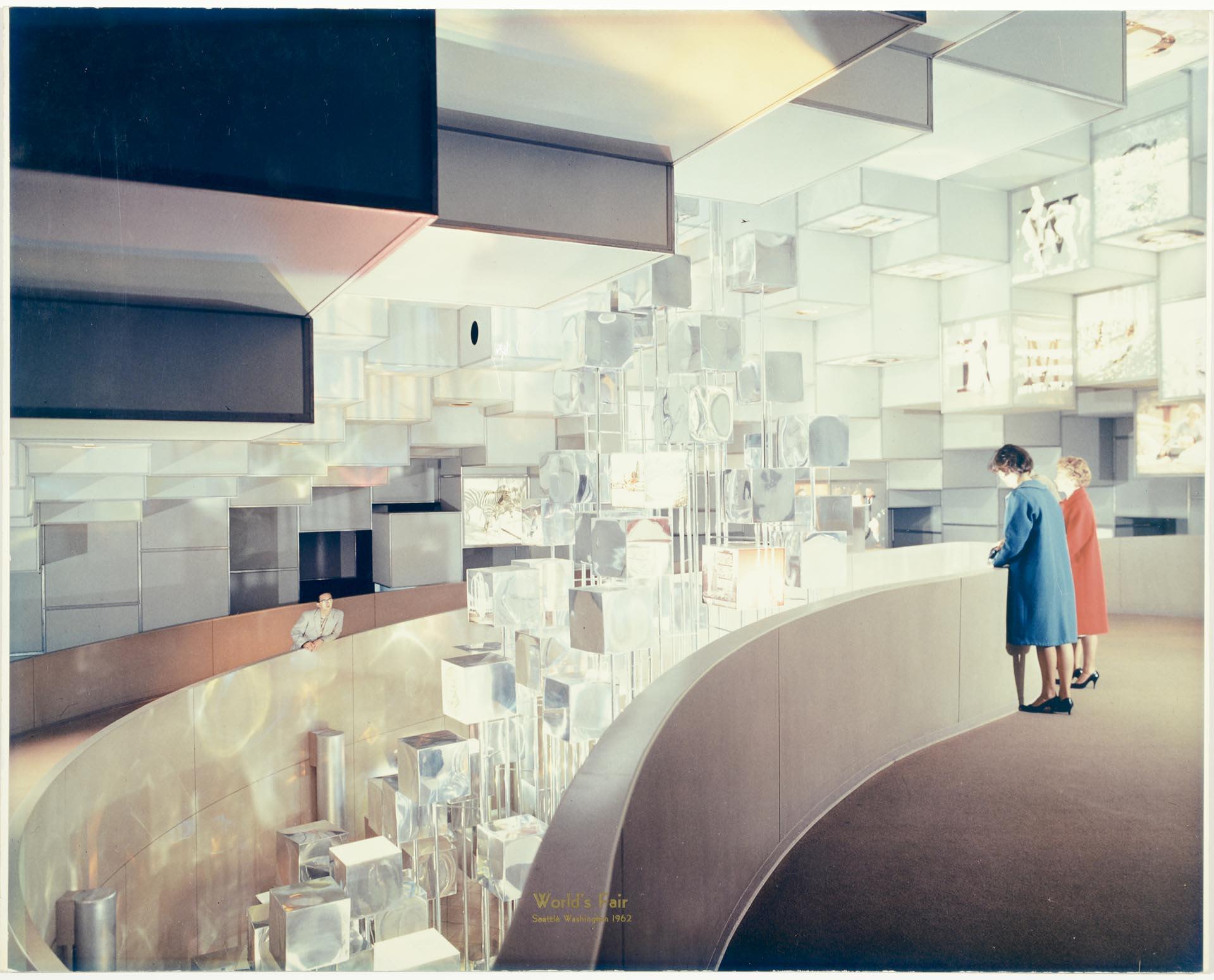 A painting of the interior of an exhibit showing two people looking over a balcony at floating geometric shapes.