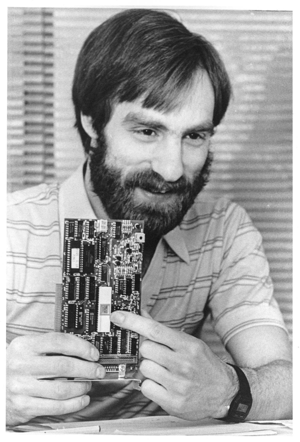 A person with a beard holds up a circuit board.