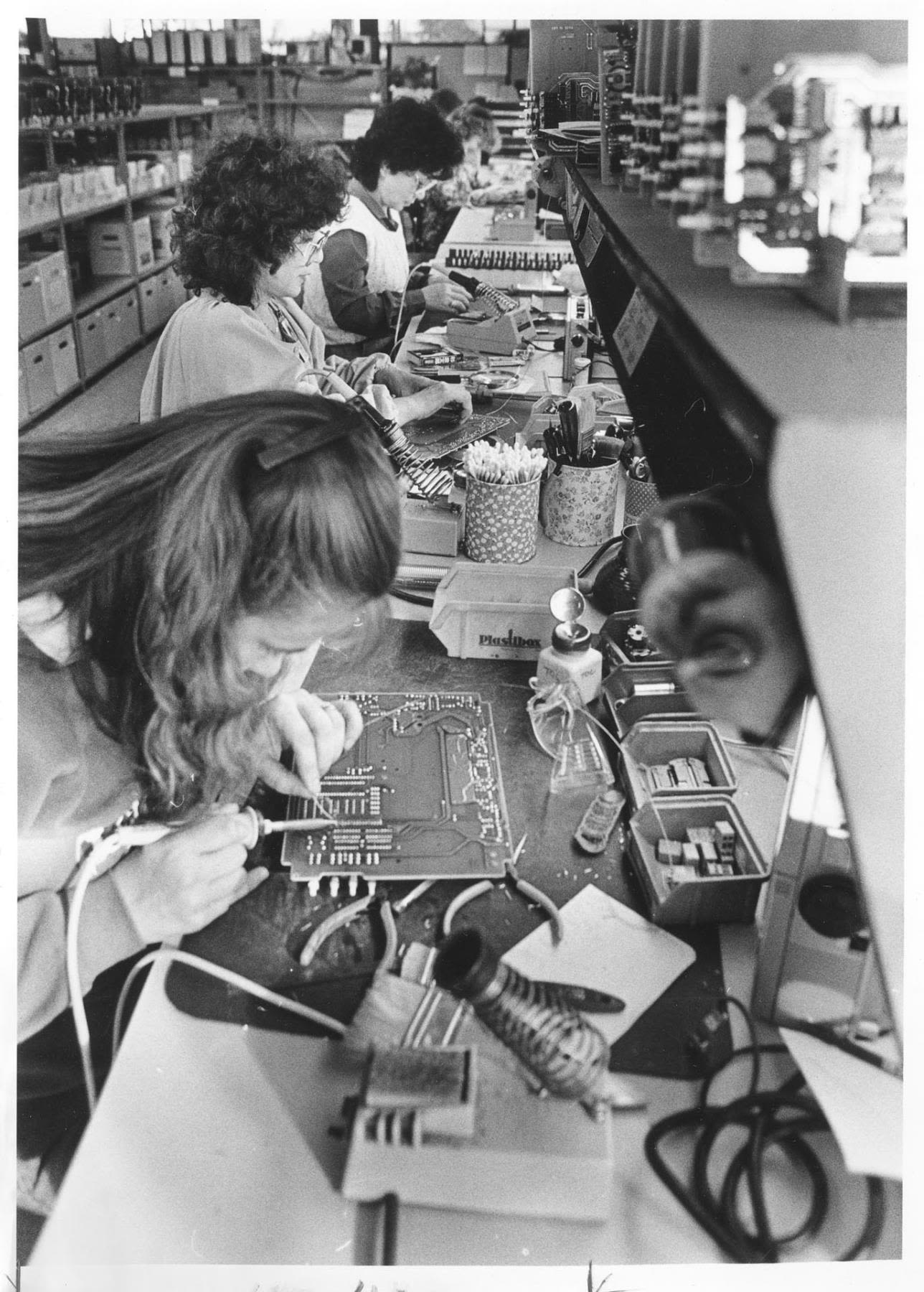 Several people assemble electronics at a work bench.